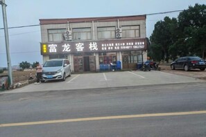 A building with a signboard, a parking area, and a few parked vehicles.