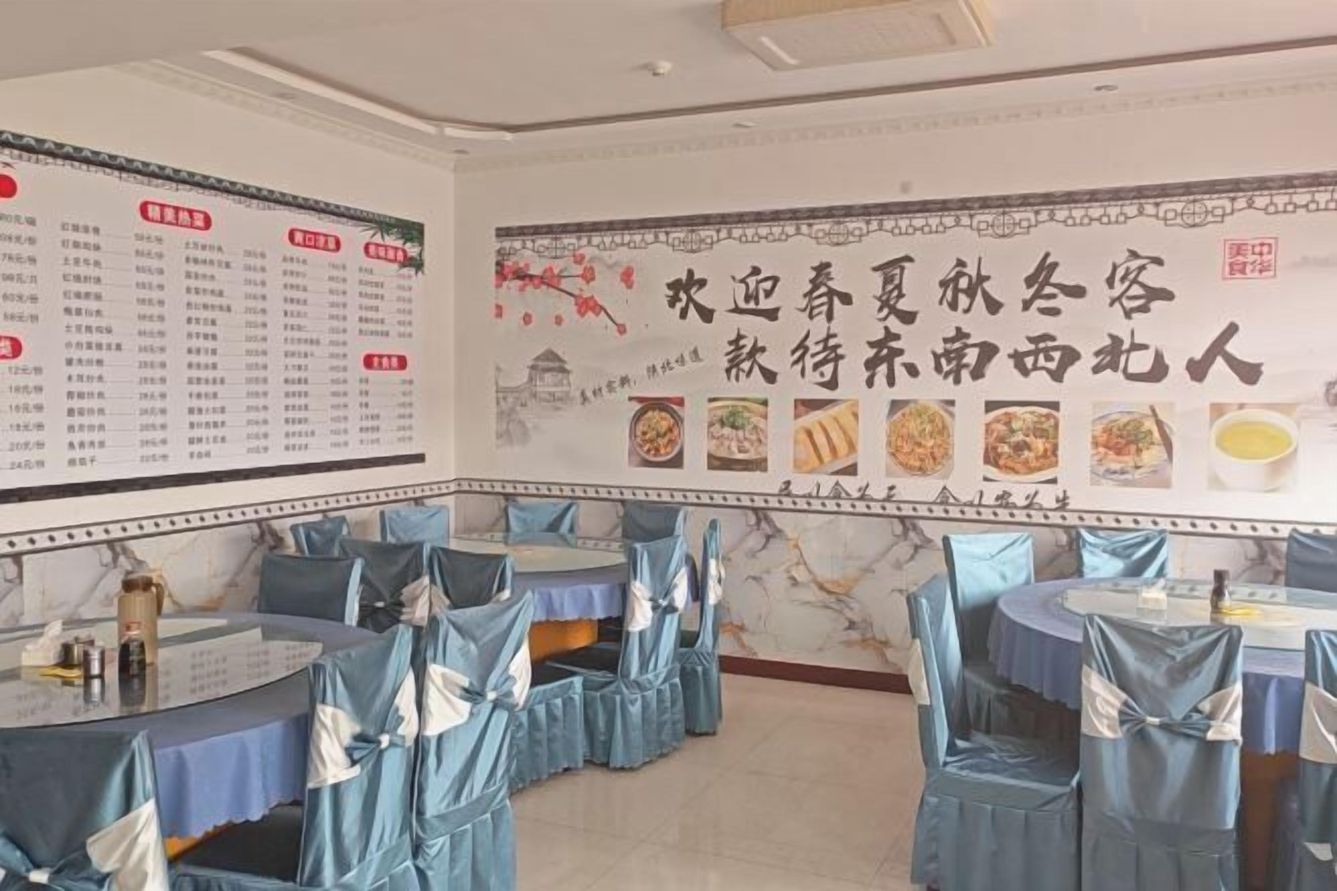 A restaurant with tables covered in blue tablecloths and chairs with blue sashes. There are menus on the walls and a large decorative banner with food images.