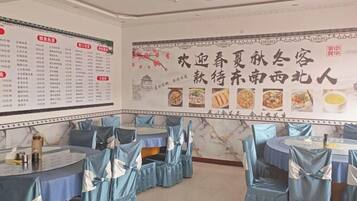 A restaurant with tables covered in blue tablecloths and chairs with blue sashes. There are menus on the walls and a large decorative banner with food images.