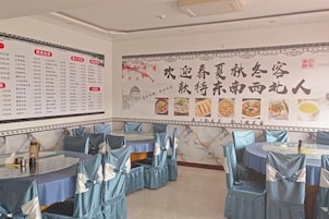 Un restaurante con mesas cubiertas con manteles azules y sillas adornadas con cintas azules. Hay menús en las paredes y un amplio cartel decorativo con imágenes de comida.