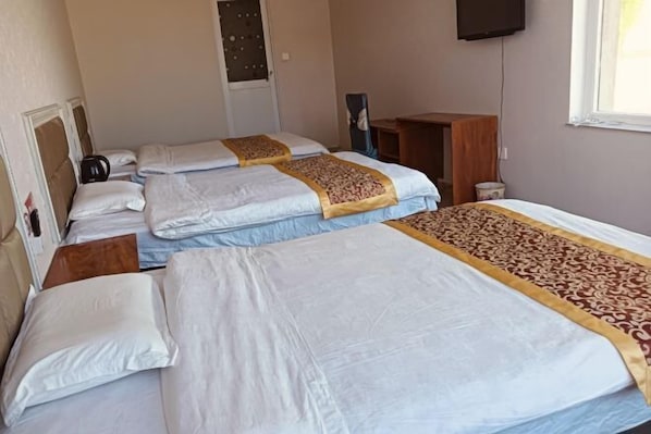 A hotel room with three beds, a television, and a window.