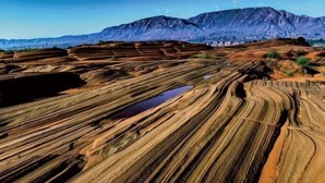 Paisagem com formações rochosas em camadas e turbinas eólicas ao longe.