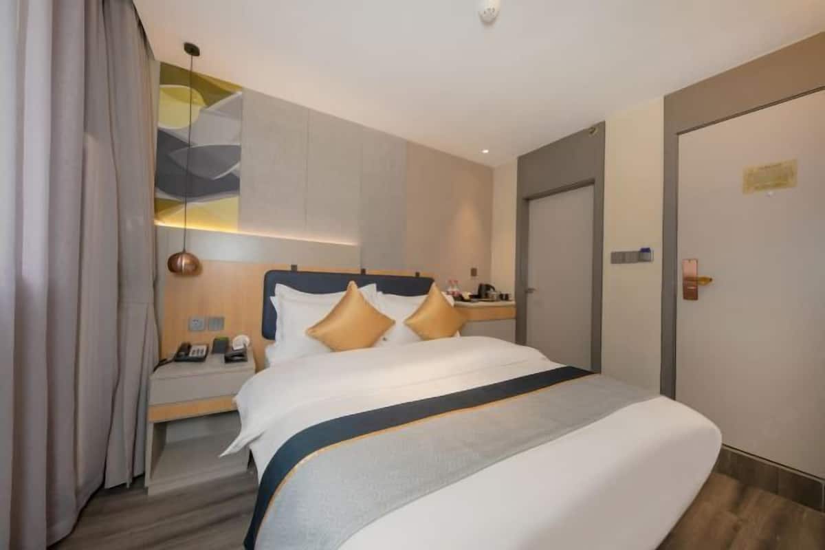 Habitación de hotel con cama, mesita de noche, lámpara, puerta y pared con diseño geométrico.