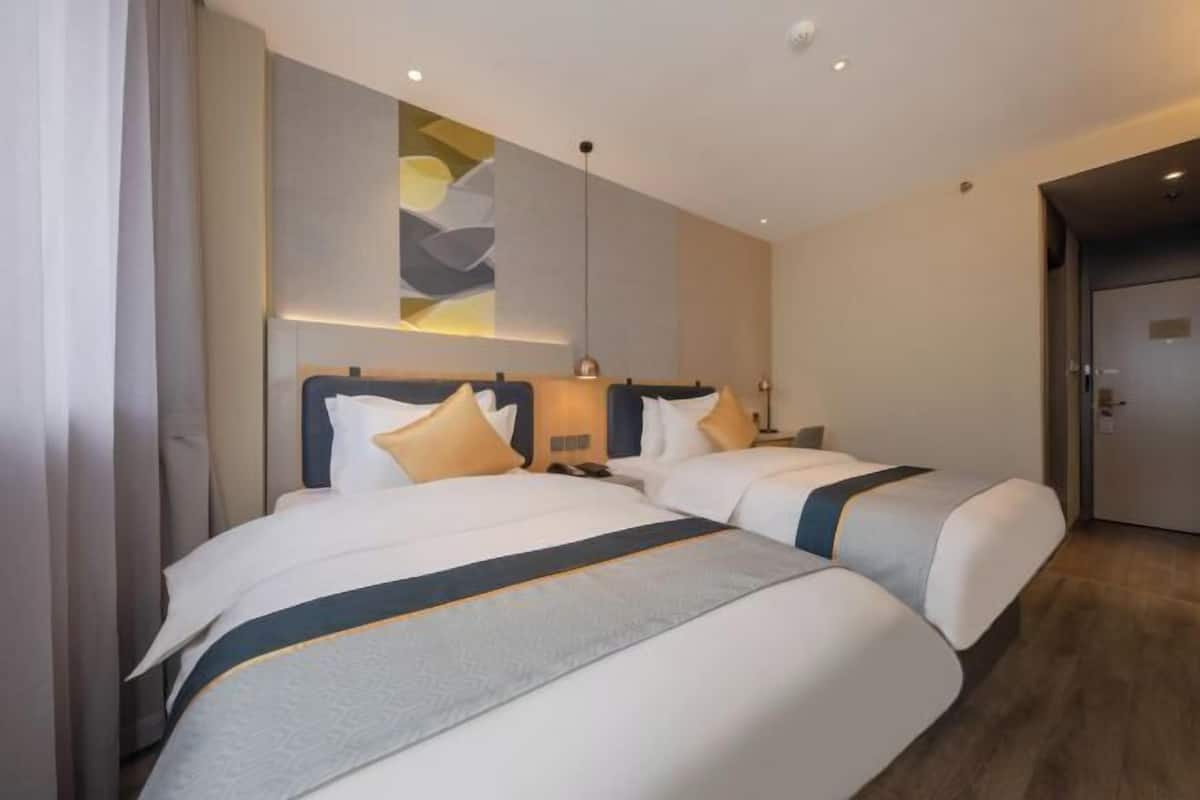 Habitación de hotel con dos camas, una lámpara moderna y una puerta.