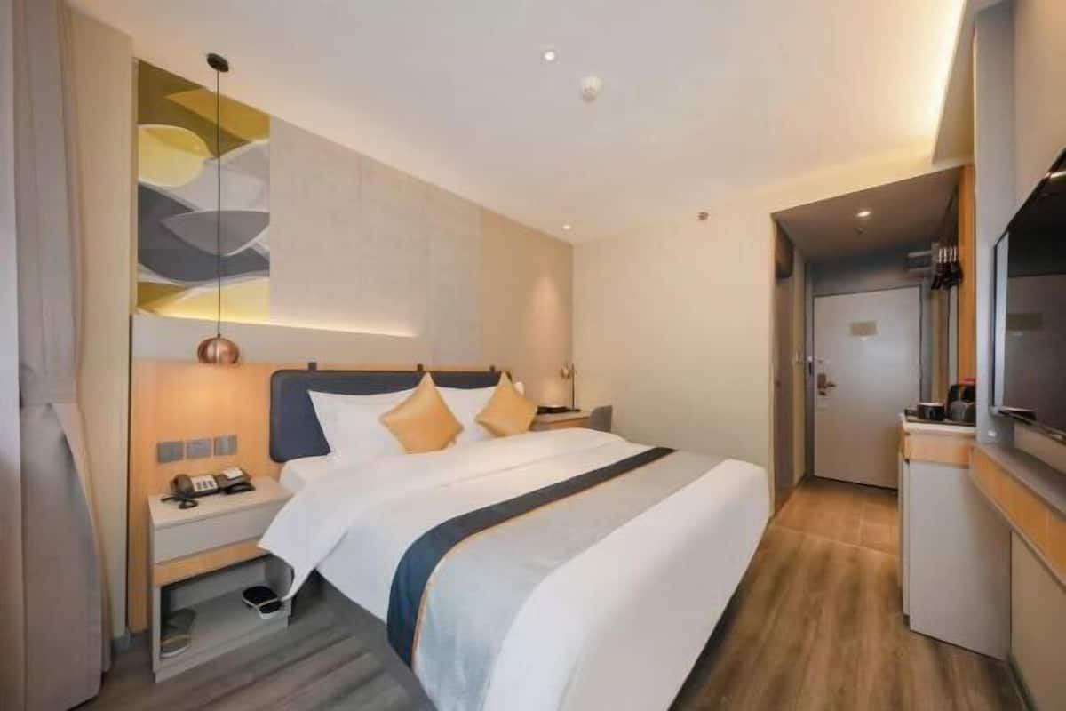 Una habitación de hotel moderna con una cama grande, mesitas de noche, un escritorio y un televisor.