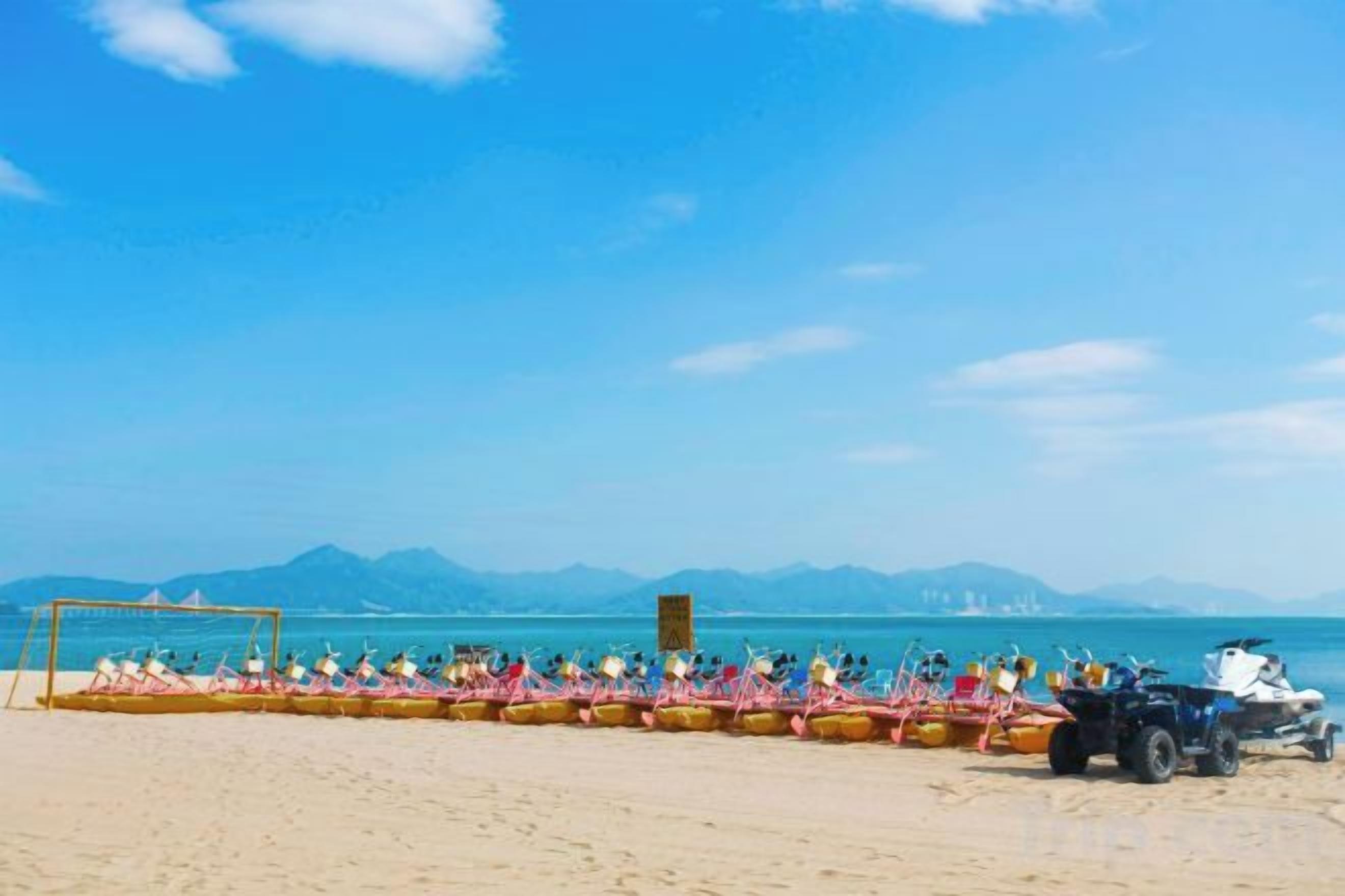 A beach with a row of boats and a dune buggy parked on the sand.