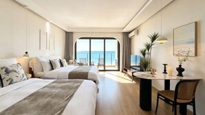 Une chambre d’hôtel avec deux lits, un bureau, une chaise, une télévision et un balcon avec vue sur la mer.