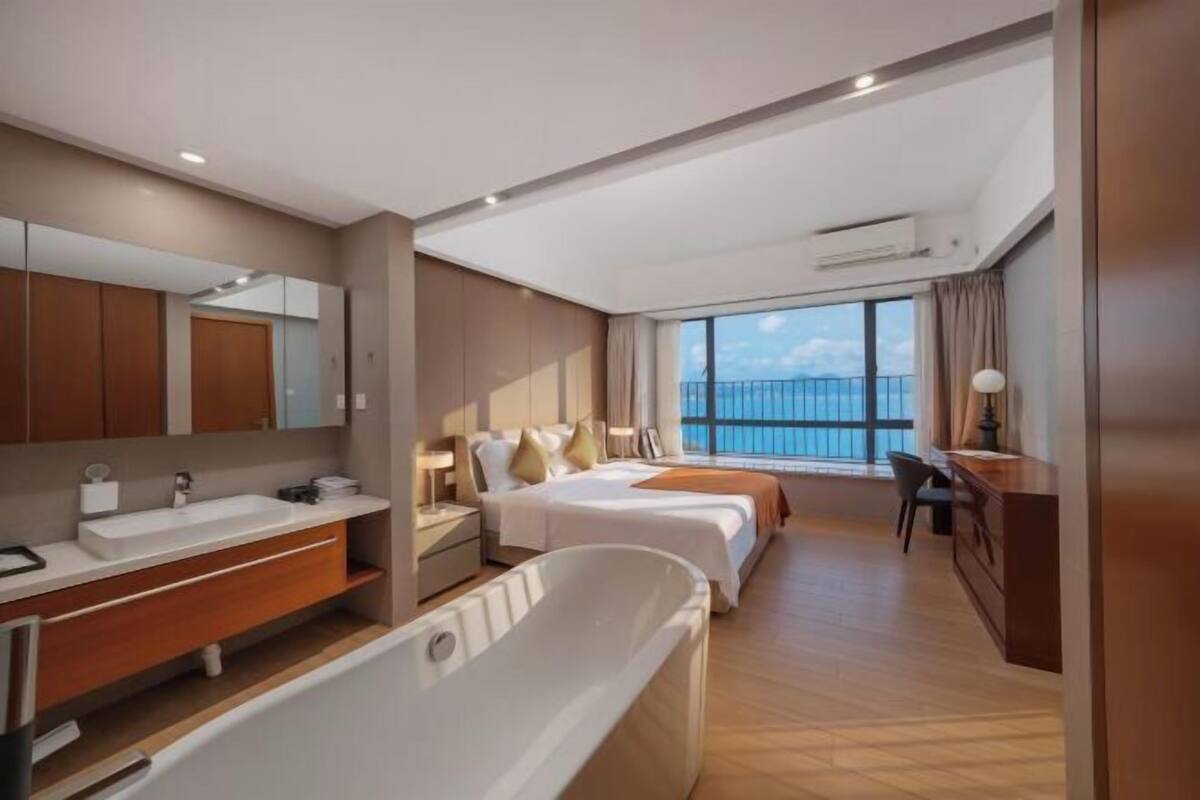 Habitación de hotel moderna con una bañera grande, dos camas, un escritorio y vista al mar.