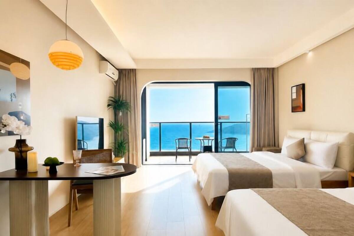Habitación de hotel con balcón, escritorio, dos camas y vista al mar.