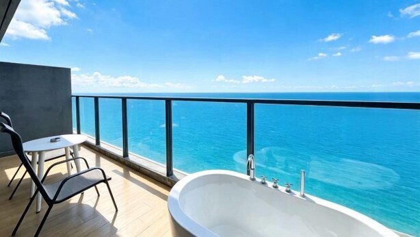 Een balkon met uitzicht op de oceaan, een witte badkuip en twee stoelen.