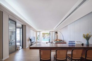 Una habitación de hotel moderna con una amplia mesa de madera, sillas de mimbre, un sofá y vista a una piscina.