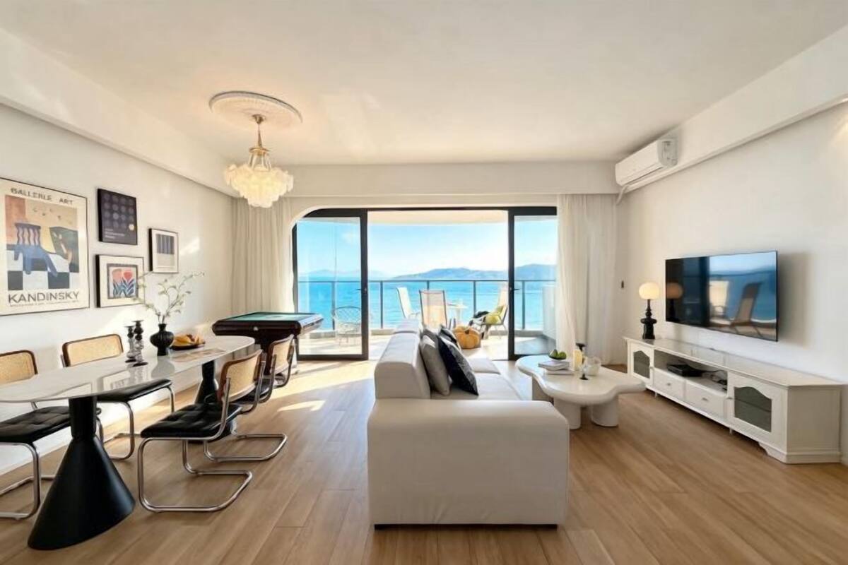 Una sala de estar moderna con una mesa de billar, un sofá, un televisor y un ventanal con vista al mar.