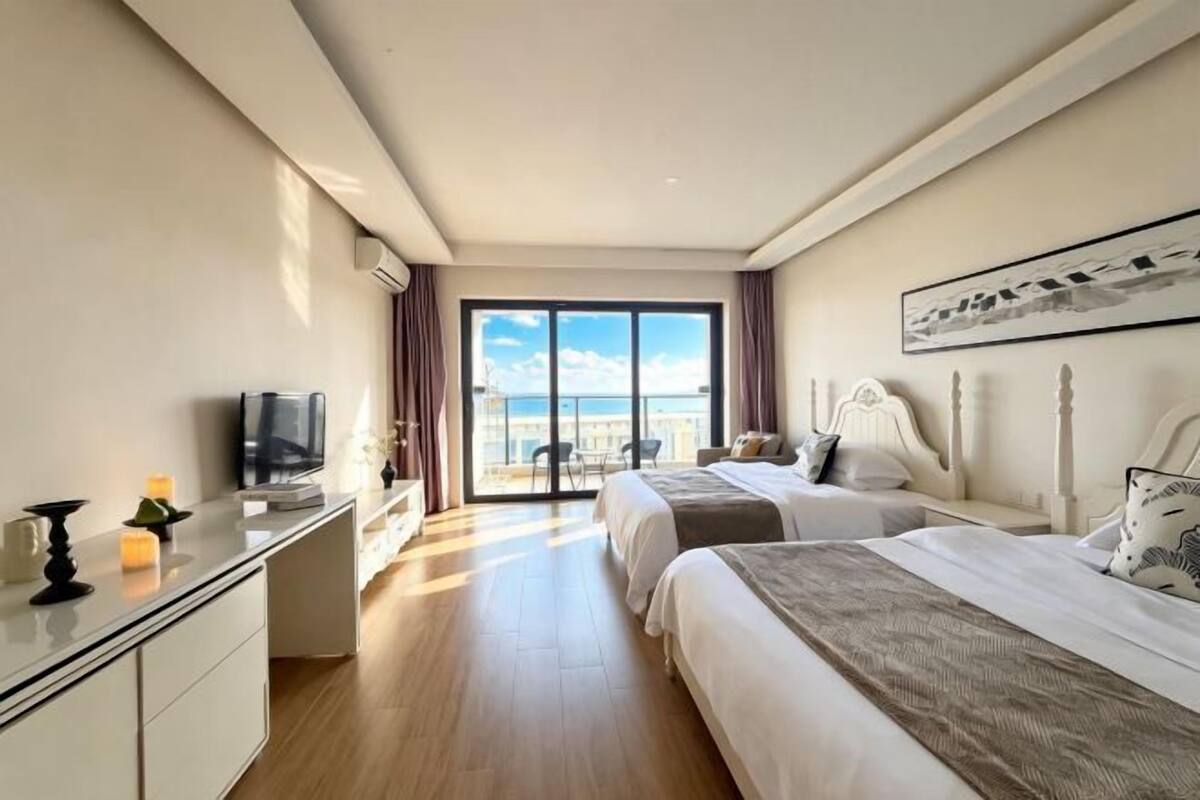 Habitación de hotel con dos camas, un escritorio, un televisor y un ventanal con vista a la ciudad.