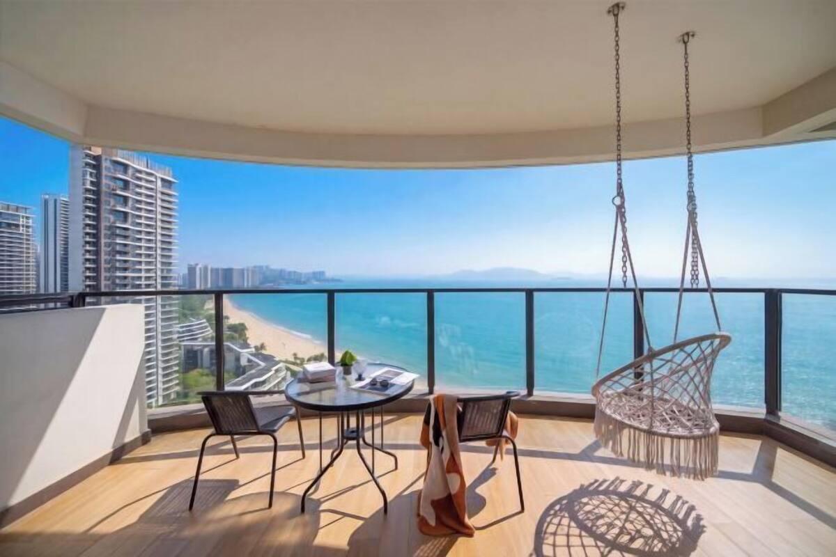 Un balcón con mesa y sillas, una silla colgante y vistas al océano y edificios.
