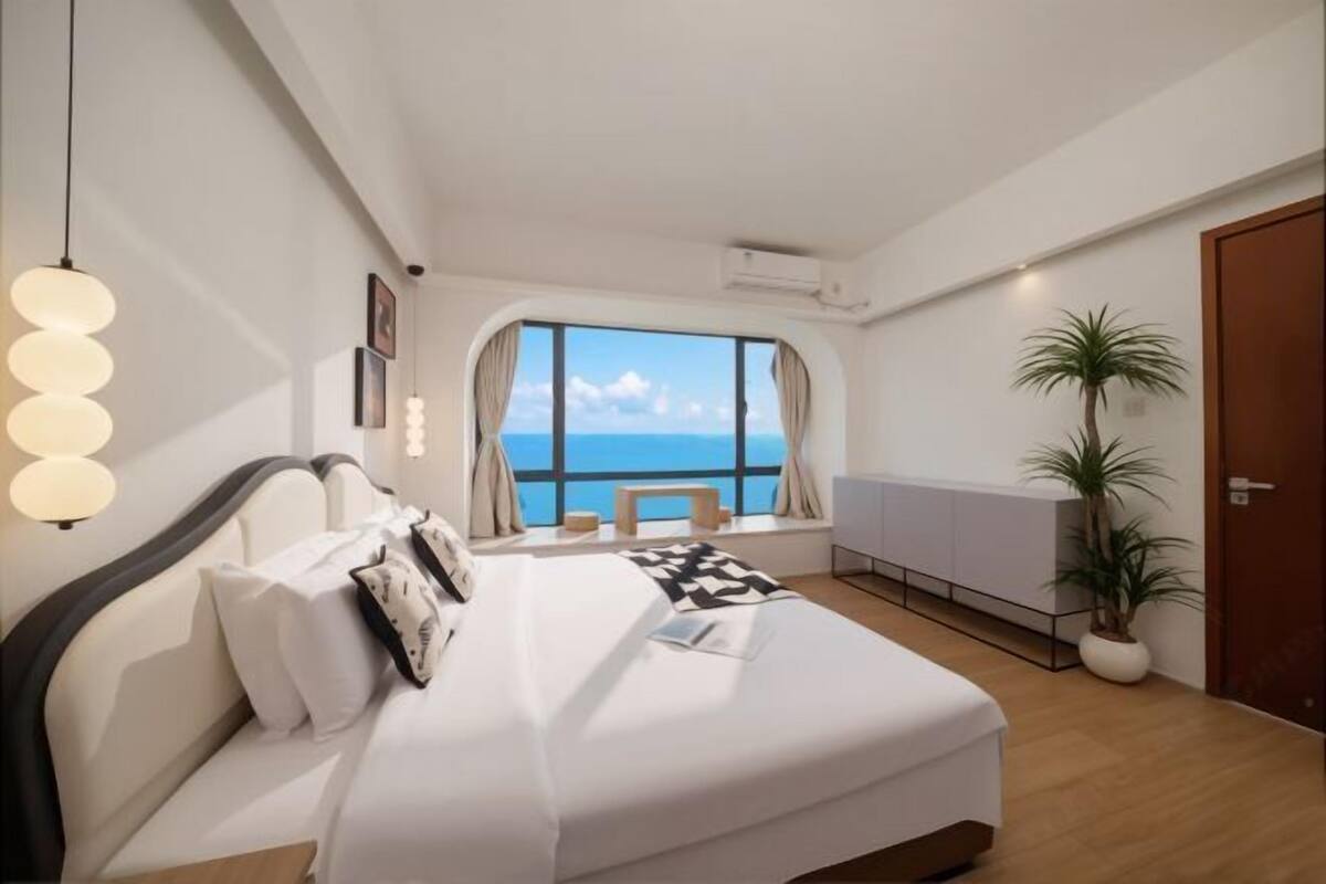 Una habitación de hotel moderna con una cama, vista al mar, una planta en maceta y una ventana con cortinas.