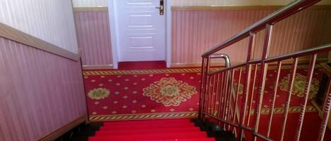A staircase with red carpeted steps and a metal railing, leading to a white door.