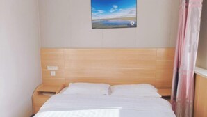 A neatly made bed with white linens, a wooden headboard, and a small bedside table. - Prairie Pearl Express Hotel (Hexigten Banner)
