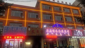 A multi-story building with illuminated signage, a visible entrance, and air conditioning units on the exterior.