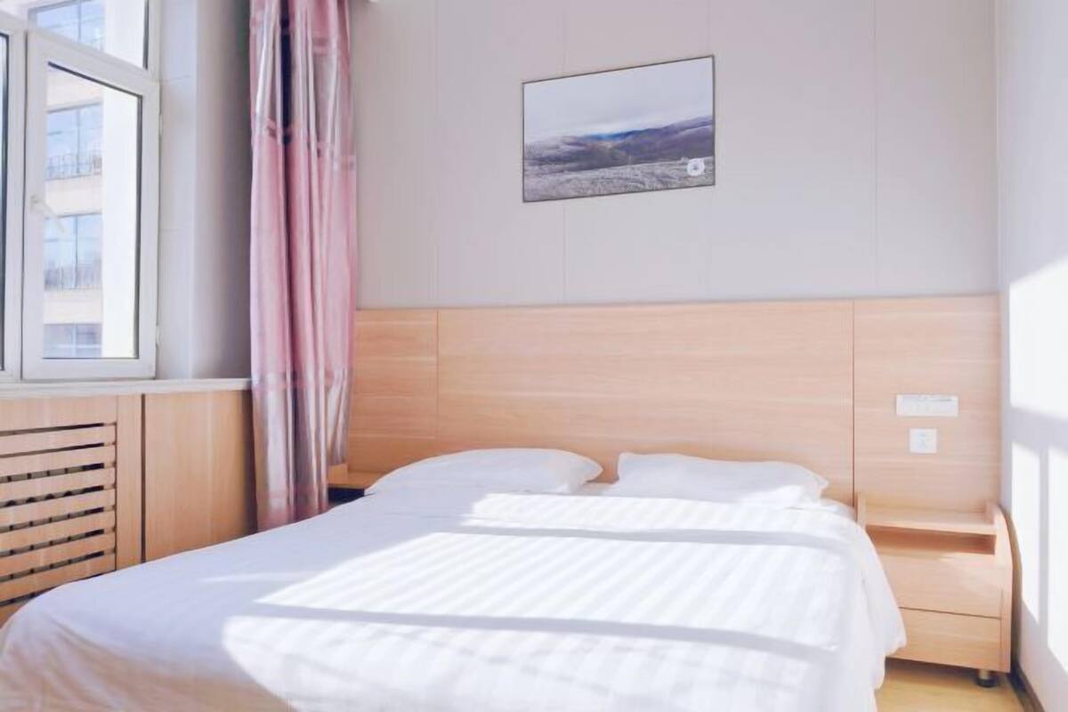 A hotel room with a bed, a window with curtains, a wall-mounted TV, and a framed picture.