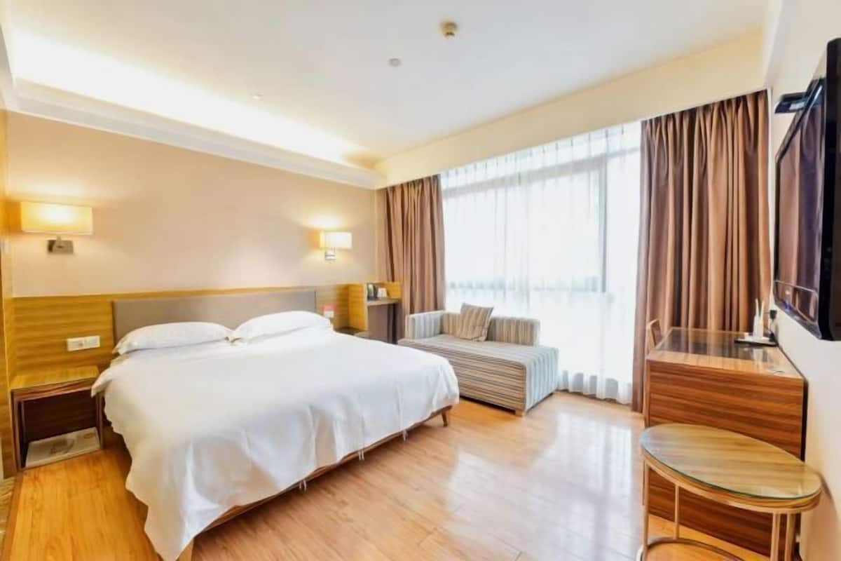 Habitación de hotel con cama, mesitas de noche, sofá, televisión y ventana con cortinas.