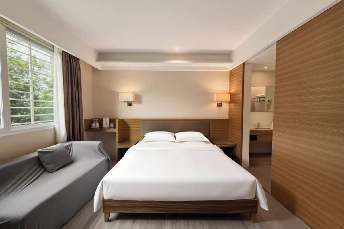Una habitación de hotel moderna con una cama grande, un sofá, una mesita de noche y una mesita auxiliar.
