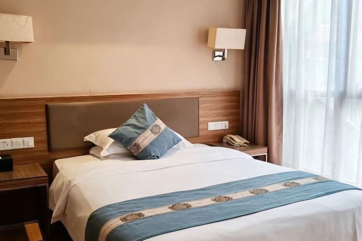 Una habitación de hotel con cama, mesita de noche, lámpara y cortinas.