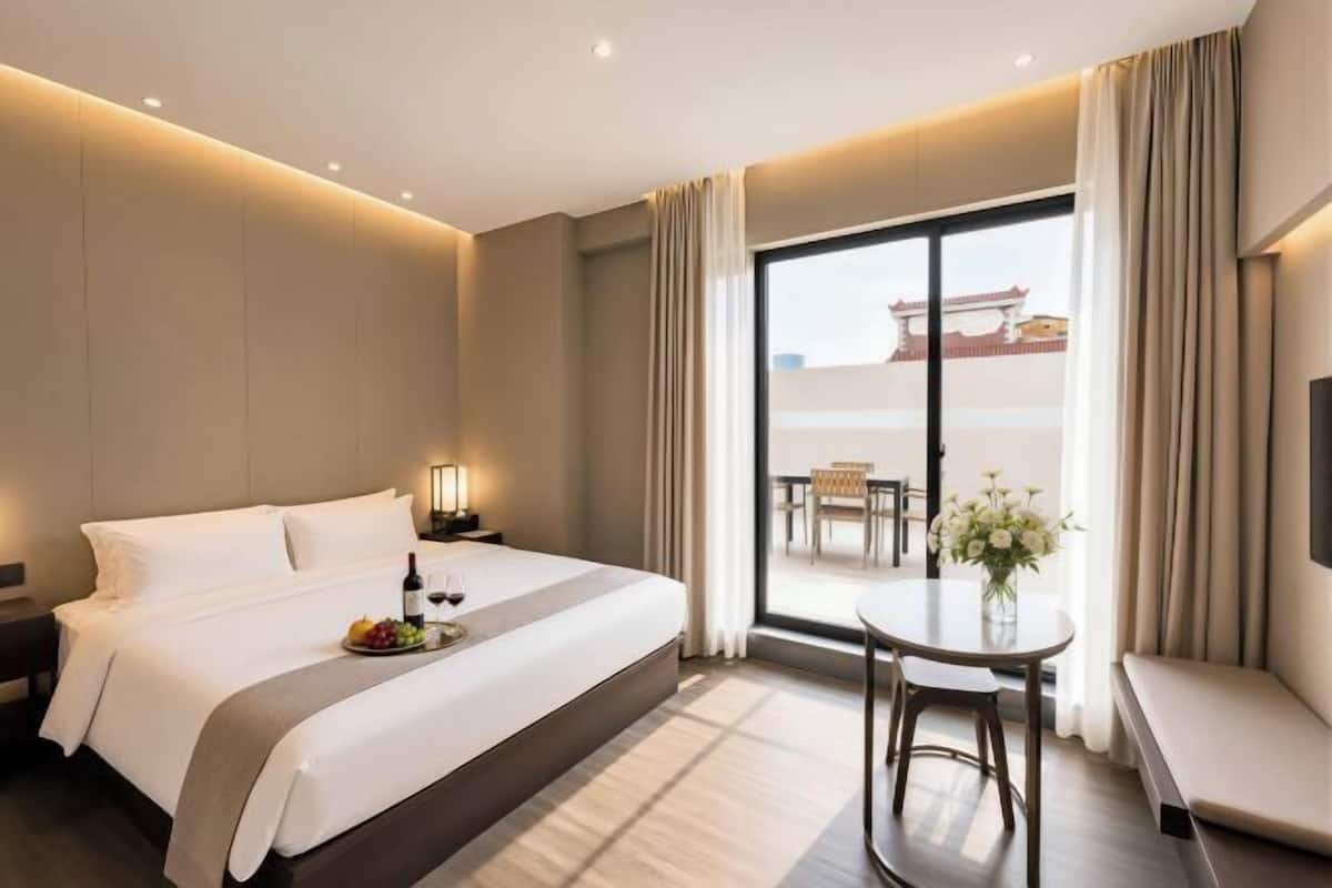 Una habitación de hotel con una cama grande, una mesita con un florero y un balcón con vistas.