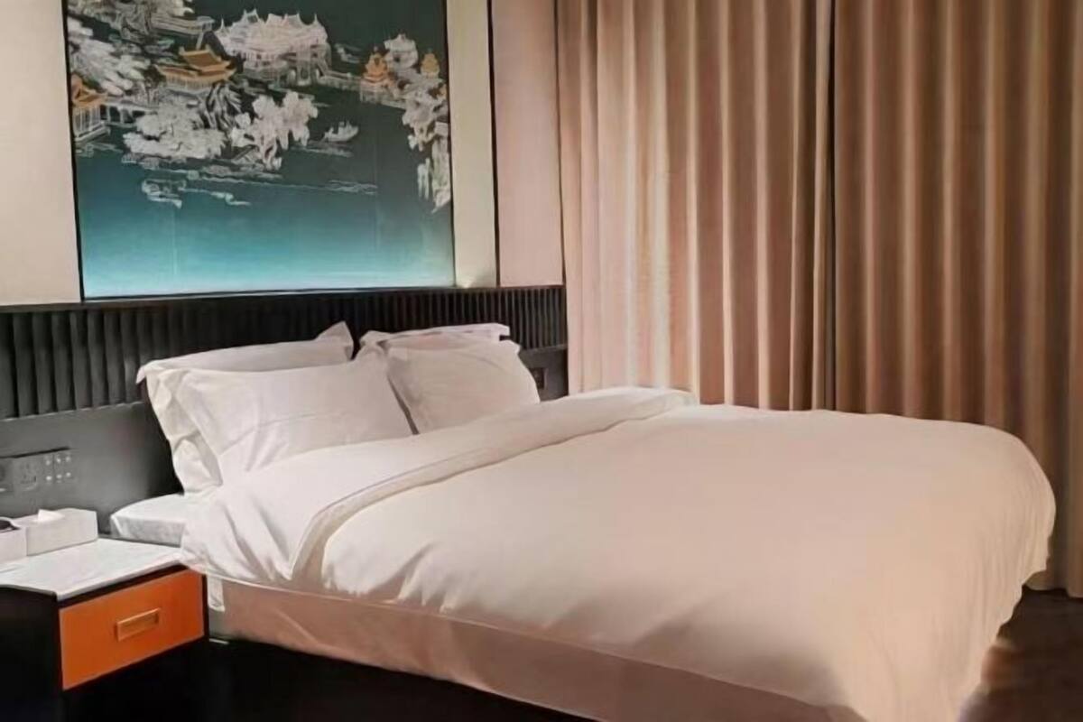 Una habitación de hotel con una cama, una mesita de noche, un cuadro en la pared y una ventana con cortinas.