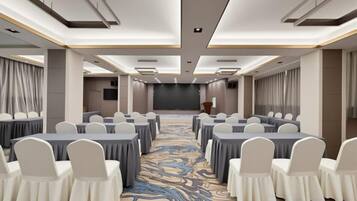 A conference room with rows of tables and chairs, a stage, and a carpeted floor.