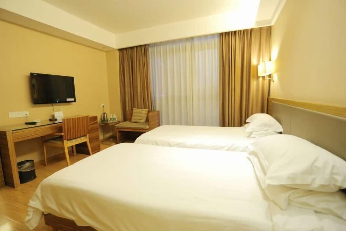 Habitación de hotel con dos camas, un escritorio con silla, televisión y ventana con cortinas.