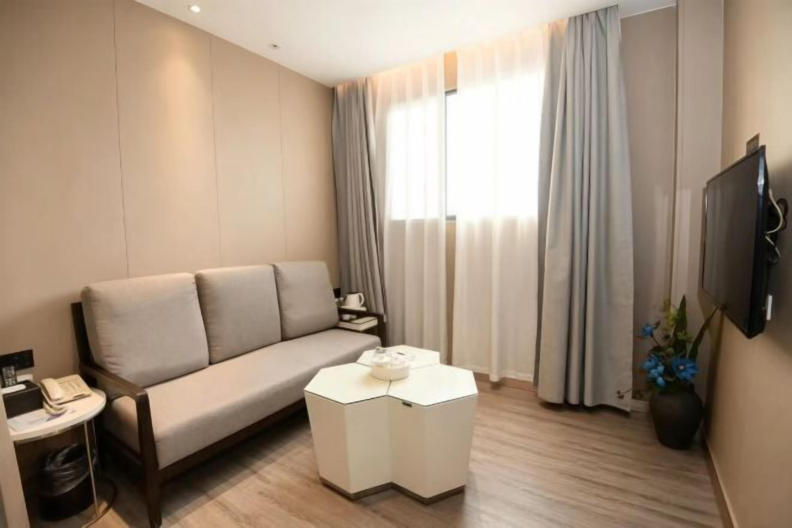 Ein Hotelzimmer mit einer Couch, einem kleinen Tisch, einem Fernseher und einem Fenster mit Vorhängen.