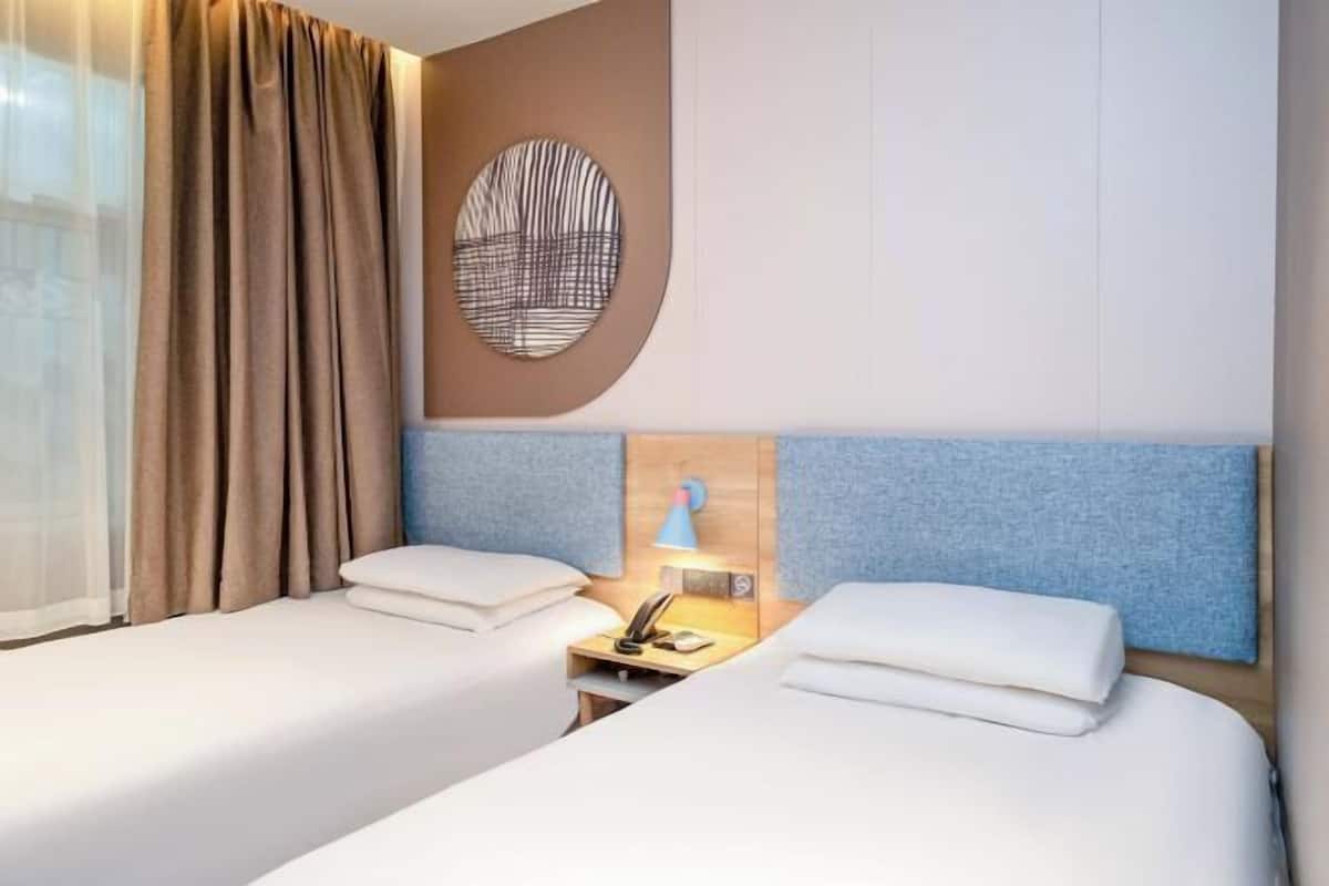 A hotel room with two beds, a wall-mounted lamp, and a circular wall decoration.