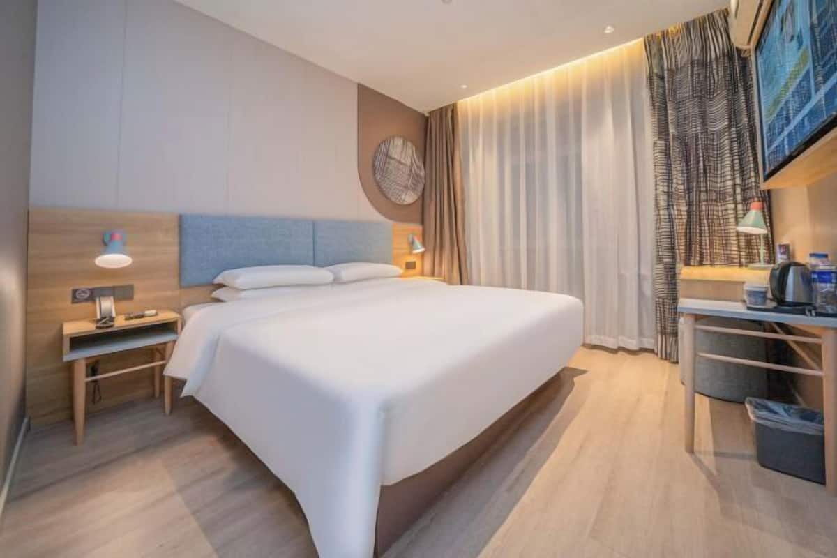 A modern hotel room with a large bed, a desk, and a wall-mounted TV.