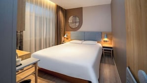 Une chambre d’hôtel avec un lit, des tables de chevet, un bureau et une grande fenêtre avec des rideaux.