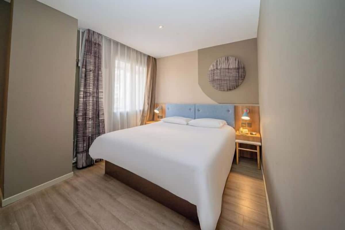 A hotel room with a large bed, bedside lamps, a round wall decoration, and a window with curtains.