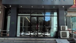 L’entrée d’un hôtel avec une façade en verre, des marches menant à l’entrée et des voitures garées en arrière-plan.