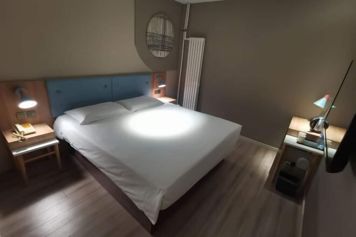 A neatly made bed with white linens, a wooden headboard, and two bedside tables with lamps.