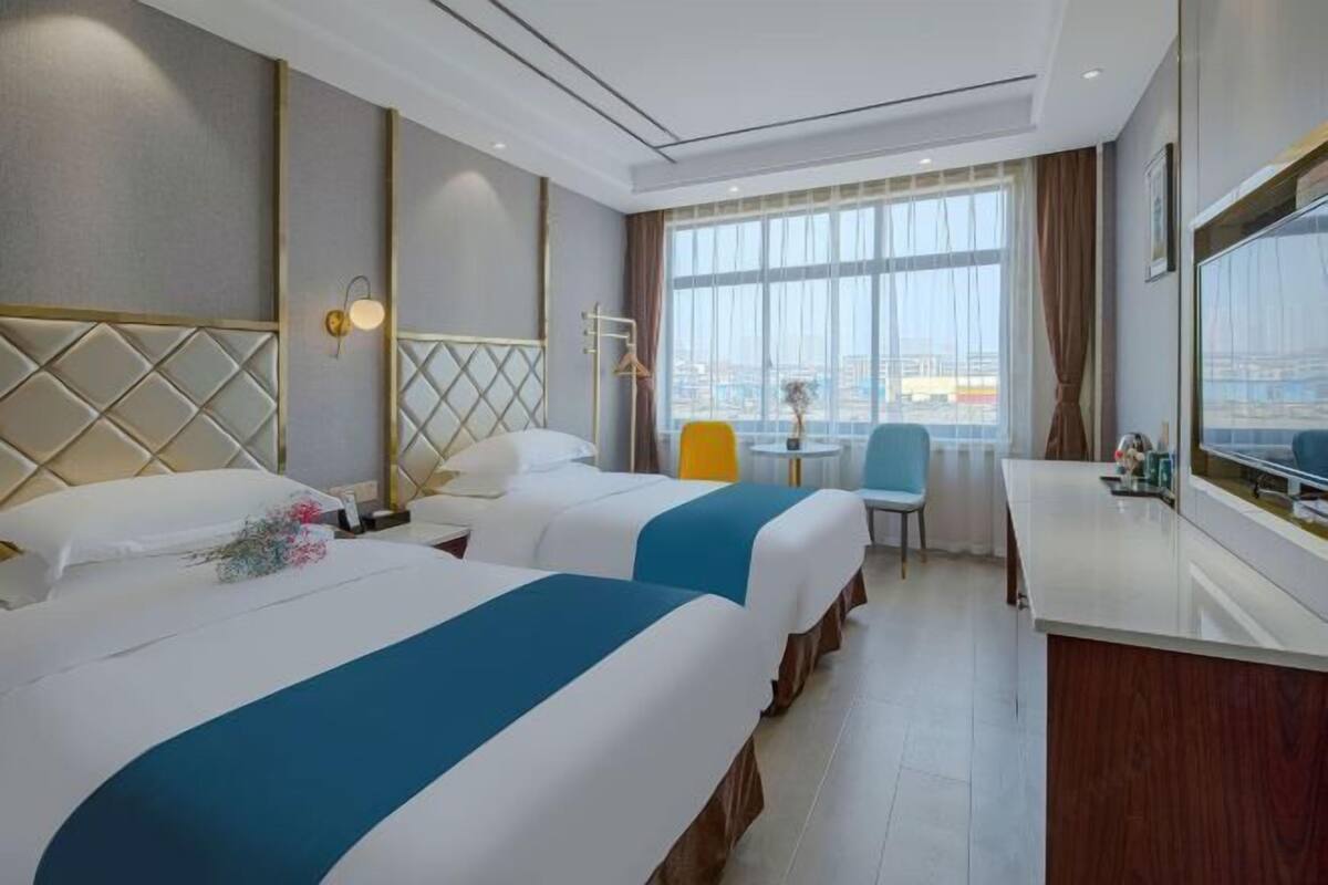 Habitación de hotel con dos camas, un escritorio, una silla y un ventanal con vistas.