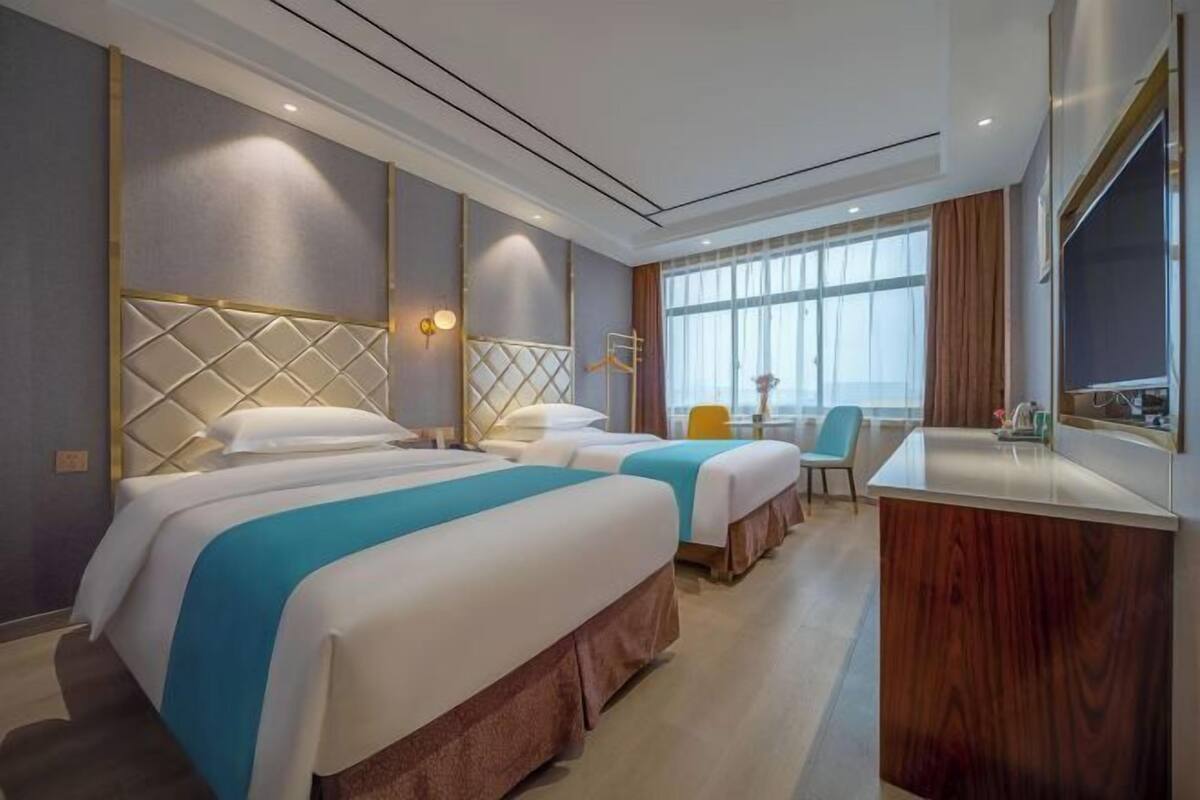 Habitación de hotel con dos camas, un escritorio, una silla y un ventanal grande.