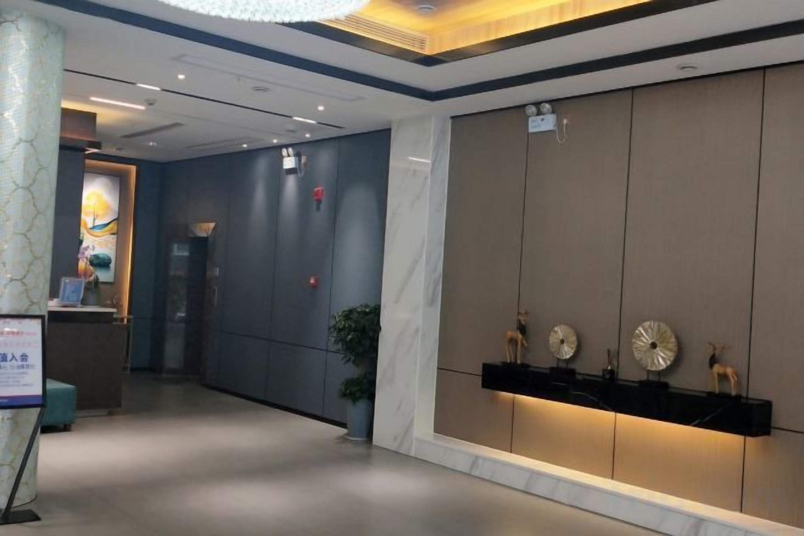 Un vestíbulo de hotel con mostrador de recepción, una planta y una pared decorada con placas.