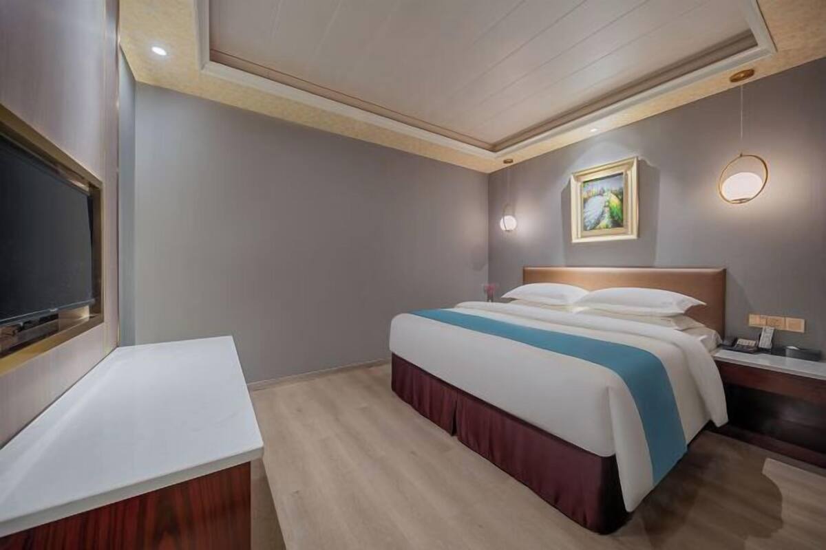 Habitación de hotel con cama, mesita de noche, televisor y un cuadro en la pared.