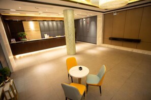 Een hotelentree met een receptiebalie, een zithoek en een grote pijler.