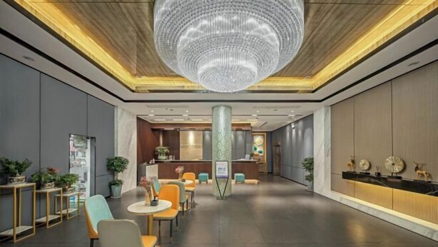 Een moderne hotellobby met een grote kroonluchter, een zithoek, een receptiebalie en decoratieve wandelementen.