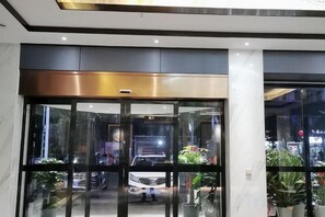 Een hotelentree met een glazen deur, metalen frame en een plafond met inbouwverlichting.