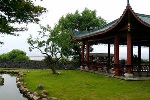 Een traditioneel paviljoen met een pannendak, omgeven door een stenen muur en een kleine vijver.