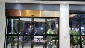 Een moderne hotelentree met een glazen deur, plantenbakken en een uitzicht op de straat.