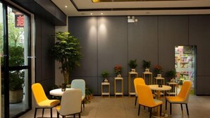 Een modern interieur met gele en witte stoelen rond tafels, een grote potplant en een uitzicht op een boekwinkel door een glazen deur.