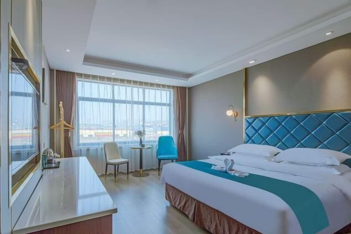 Una habitación de hotel con cama, escritorio, silla, mesita y ventana con cortinas.