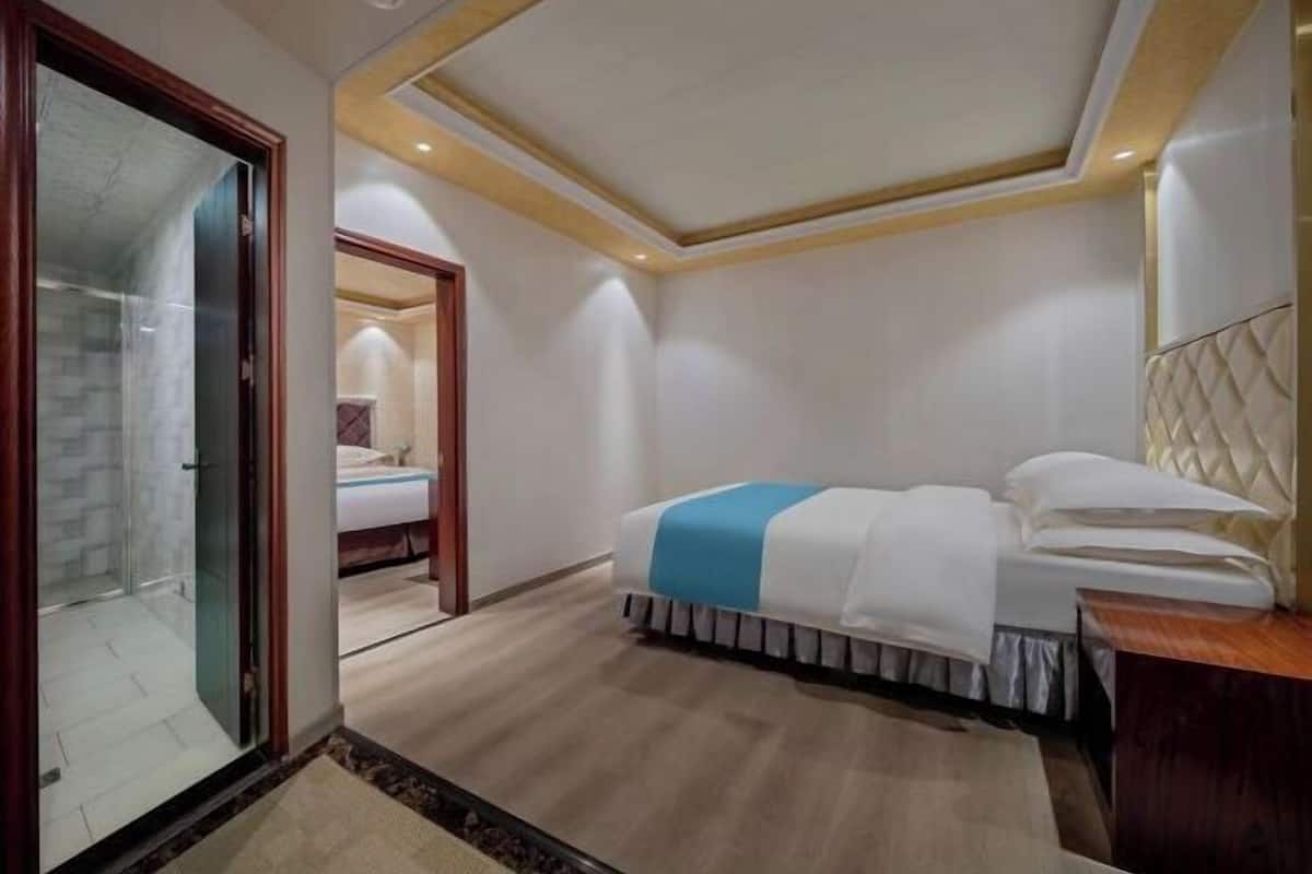 Una habitación de hotel con cama, cabecero de madera, box de ducha de vidrio y piso de madera.