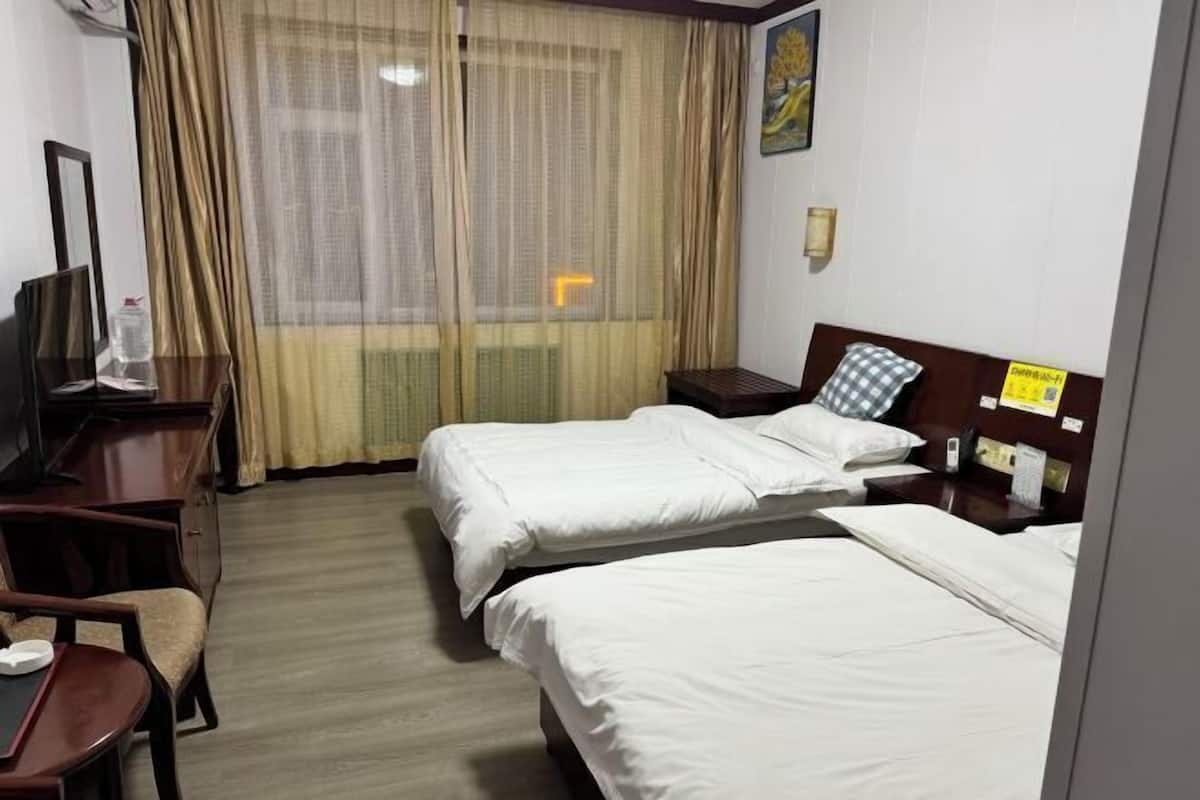 A hotel room with two beds, a desk, a chair, a TV, and a window with curtains.
